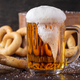 Foamy pint glass of beer surrounded by pretzels
